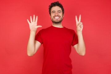 Young handsome caucasian man wearing t-shirt over isolated red background showing and pointing up with fingers number seven while smiling confident and happy.