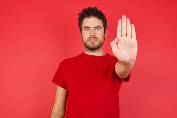 Fototapeta premium Young handsome caucasian man wearing t-shirt over isolated red background doing stop gesture with palm of the hand. Warning expression with negative and serious gesture on the face