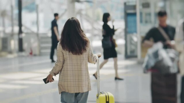 View from back of businesswoman moving along airport terminal with smartphone in hand. Young woman walking with suitcase and checking news or chatting over phone. Concept of travel, technology.