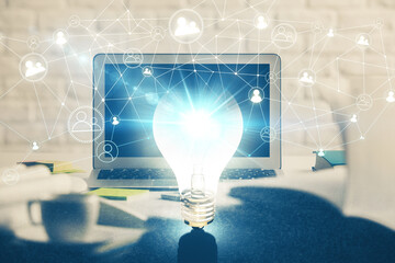 Computer on desktop in office with bulb icon hologram. Double exposure. Concept of idea.
