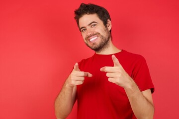 Young handsome caucasian man wearing t-shirt over isolated red background pointing fingers to camera with happy and funny face. Good energy and vibes.