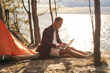 Cheerful man using laptop during camping in nature