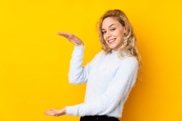 Young blonde woman isolated on yellow background holding copyspace to insert an ad
