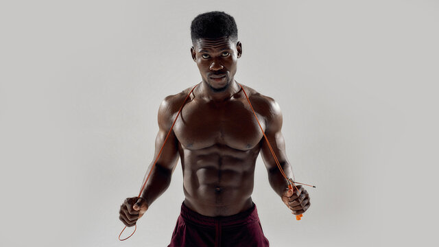 Young muscular african american man looking at camera, while holding jumping rope isolated over grey background. Sports, workout, bodybuilding concept