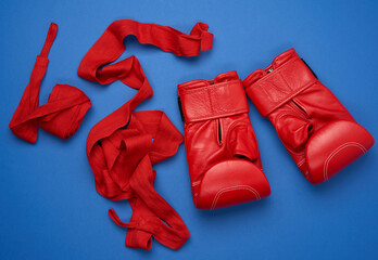 pair of red leather boxing gloves and a textile red elastic bandage for hands lie on a blue background