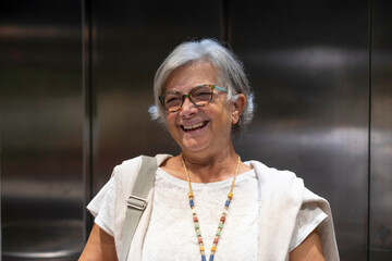 A cheerful senior woman inside an elevator laughing amused for something funny. Active retired elderly people and fun concept. © luciano