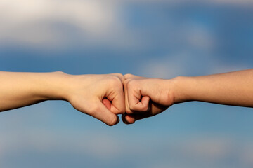 Two female hands doing fist bump over blue sky background