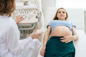 Female doctor examines abdominal of belly of lying pregnant young woman. Female doctor is using transducer for sonogram screening of pregnant girl in medical clinic.