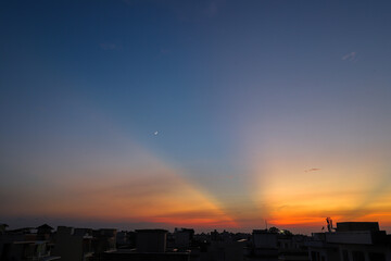 A breathtaking view of a city captured during sunset with colorful clouds and moon