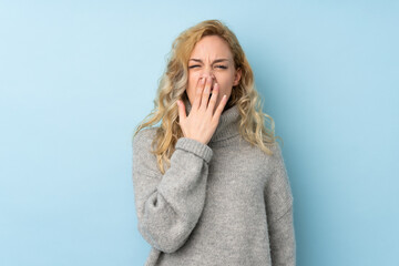 Young blonde woman wearing a sweater isolated on blue background yawning