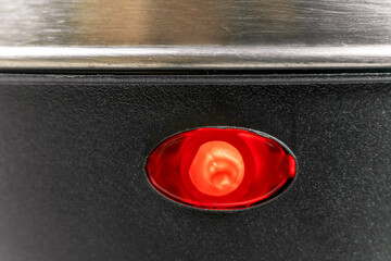 Lower half of a grey electric kettle with a red light on, macrophotograph