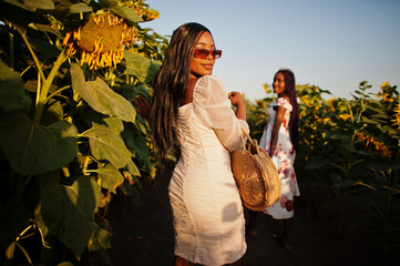 Two pretty young black friends woman wear summer dress pose in a sunflower field.