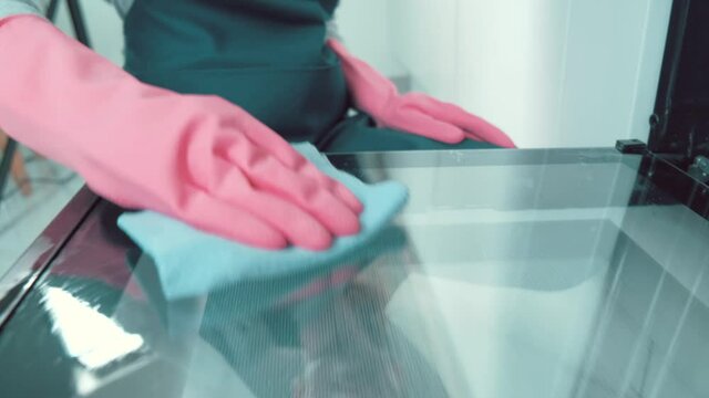 The girl wipes the kitchen door inside the oven with a rag. Girl in pink rubber gloves.