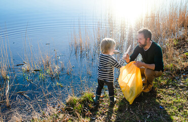 Father with small son collecting rubbish outdoors in nature, plogging concept.
