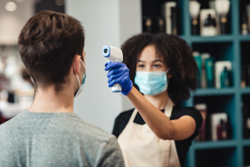 Fototapeta premium Close up of woman barber making temperature screening on client at barbershop