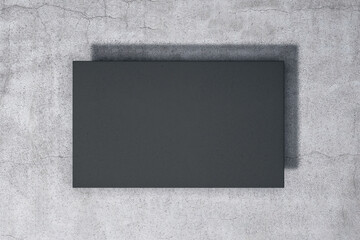 Empty black poster hanging on concrete wall.
