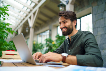 Young man with laptop sitting indoors in green office, working.