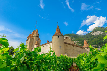 Fototapeta premium Grape leaves in foreground and rows of vines surround Chateau d'Aigle in Canton Vaud, Switzerland. Aigle Castle overlooking terraced vineyards and Swiss Alps. Wine region with popular tasting tours.