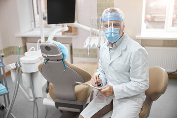 Focused dentist looking down at his notes - obrazy, fototapety, plakaty