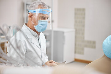 Elderly man wearing a face shield holding a tablet