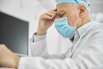 Eldelry doctor wearing a mask and looking exhausted