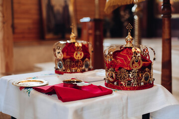 Fototapeta na wymiar Picture of two beautiful crowns with gold and red cloth stand on a table with other attributes in the church before the baptism of the baby.