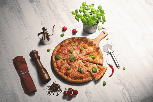 Fresh pizza with tomatoes and basil on a white washed wooden counter. Pepper grinder, pizza cutter and napkin surrounding the pizza.