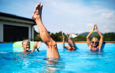 Group of seniors in swimming pool outdoors in backyard, having fun.