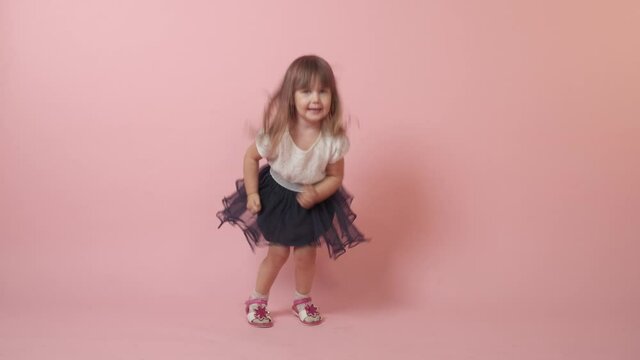Cute little brunette girl jumping and laughing. Beautiful bright festive outfit. Pink background.