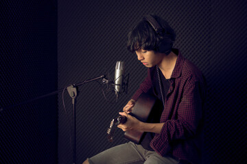 Fototapeta na wymiar Young asian man plaing guitar in front of microphone in music studio record room