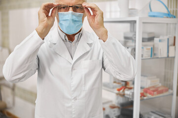 Naklejka premium Serious healthcare worker in a labcoat putting glasses on