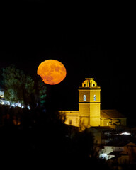 Fototapeta na wymiar Full moon rise over town, in Polop de la Marina, Alicante, Spain, full moon next to church, moon rise on the Costa Blanca