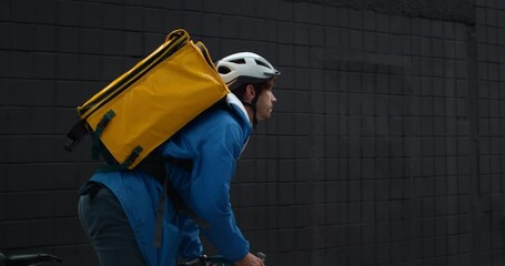 Backside view of male courier with food transportation backpack riding bicycle at street. Man in protective cycling helmet delivering order to customer. Concept of food delivery service