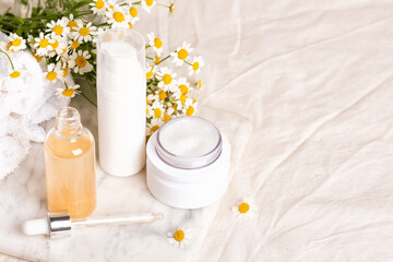 Obraz na płótnie Canvas Glass and plastic bottles of essence or serum and with chamomile flowers on marble board. Moisturizing face cream and camomile