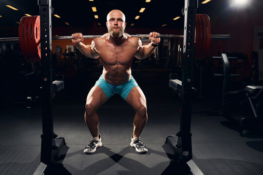 Muscular sportsman squatting with a barbell on his shoulders