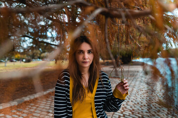 A pretty woman framed by autumnal leaves and branches at park. Looking at camera