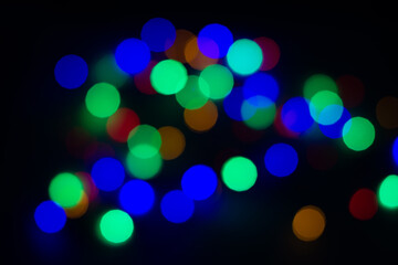 Blurry colored circles on a black background. Blurred garland on a black background, christmas background.