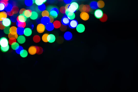 lurry colored circles on a black background. Blurred garland on a black background, christmas background. Christmas card mockup with copy space. Blurred colorful garland in the upper corner.