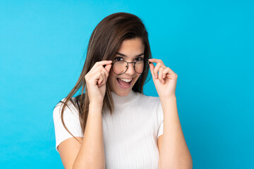 Teenager girl over isolated blue background with glasses and surprised