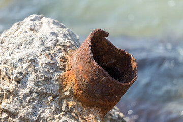 A piece of truncated, broken off rusty pipe sticks out of a piece of concrete. Metal rust is a broken construction. A piece of Rusty pipe on the sea-line. Building debris thrown ashore