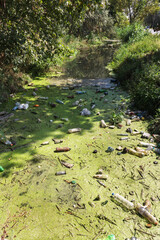 Spilled garbage to small river. Empty used dirty plastic bottles float in canal water. Pollution of environment by household waste. Ecological problem. River contaminated with various garbage