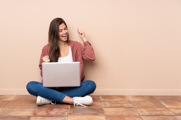 Teenager student girl sitting on the floor with a laptop celebrating a victory