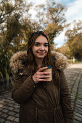 A caucasian woman smiling at camera while holding a coffee at park