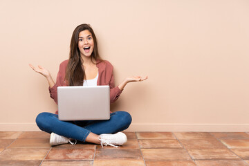 Teenager student girl sitting on the floor with a laptop with shocked facial expression
