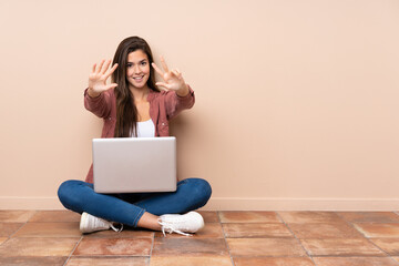 Teenager student girl sitting on the floor with a laptop counting eight with fingers