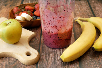Making Fruit Smoothie with banana, blueberry, strawberry and milk. Blender filled with fresh whole fruits for making a smoothie or juice