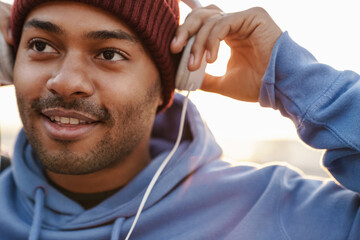 Image of pleased african american sportsman using headphones