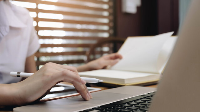 Young  woman sitting at table and taking notes in notebook.On table is laptop.