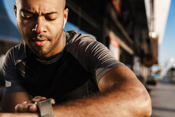 Image of concentrated african american sportsman using smartwatch