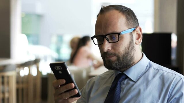 Young businessman with smartphone drinking water sitting in hotel cafe